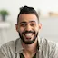 portrait of handsome young arab man smiling and looking at camera sitting on sofa at home